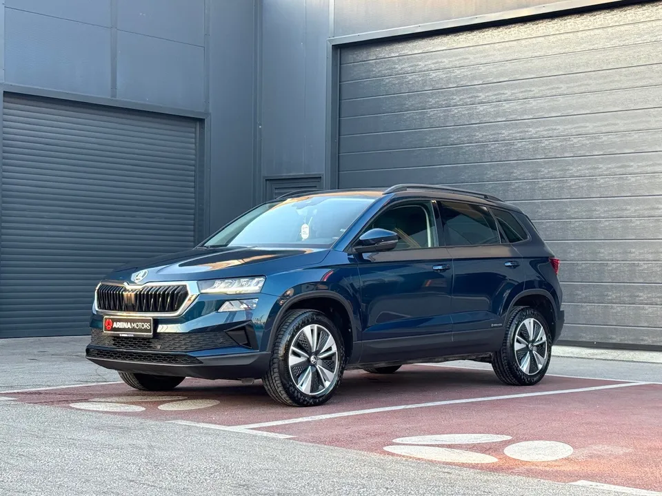 Plava Škoda Karoq snimljena sprijeda sa strane, parkirana ispred sive hale