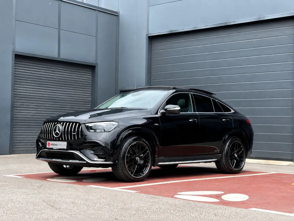 Crni Mercedes-Benz GLE 53 AMG Coupe, prednji lijevi bočni ugao, crne AMG felge, parking ispred sivih garažnih vrata