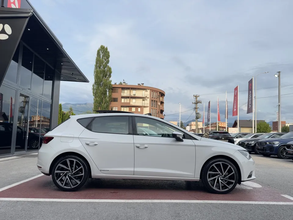 Bijeli Seat Leon, desni bok s crno-srebrnim alu felgama na parkingu