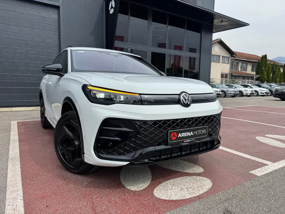 Bijeli Volkswagen Tiguan, prednji lijevi ugao s upaljenim LED dnevnim svjetlima ispred zgrade salona
