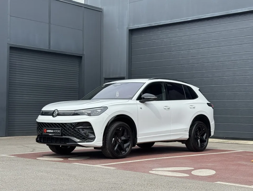Bijeli Volkswagen Tiguan R-line, prednji bočni pogled s lijeve strane, crne alu felge, ispred sive garažne hale