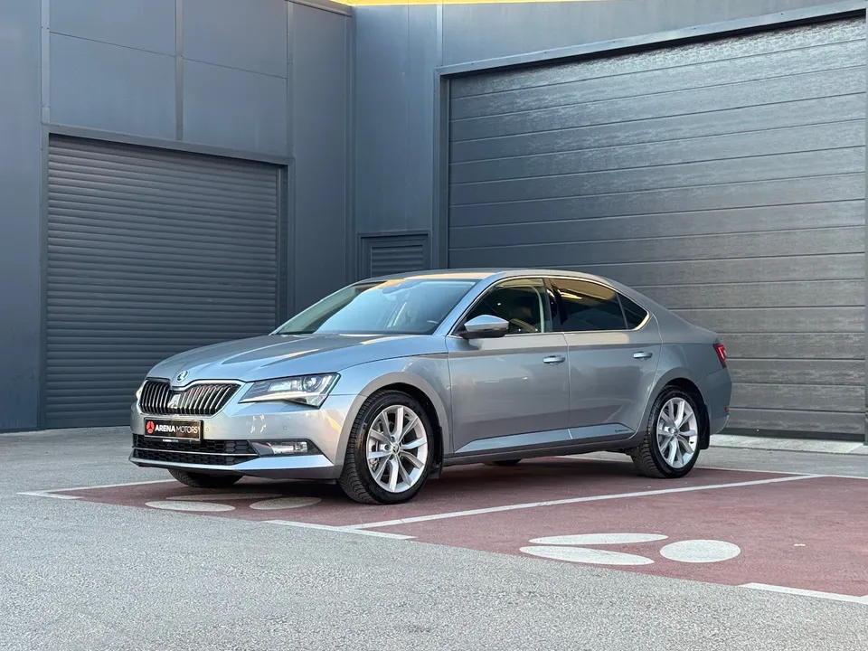 Škoda Superb, siva limuzina, prednji lijevi bočni ugao, parkirana ispred sivog objekta